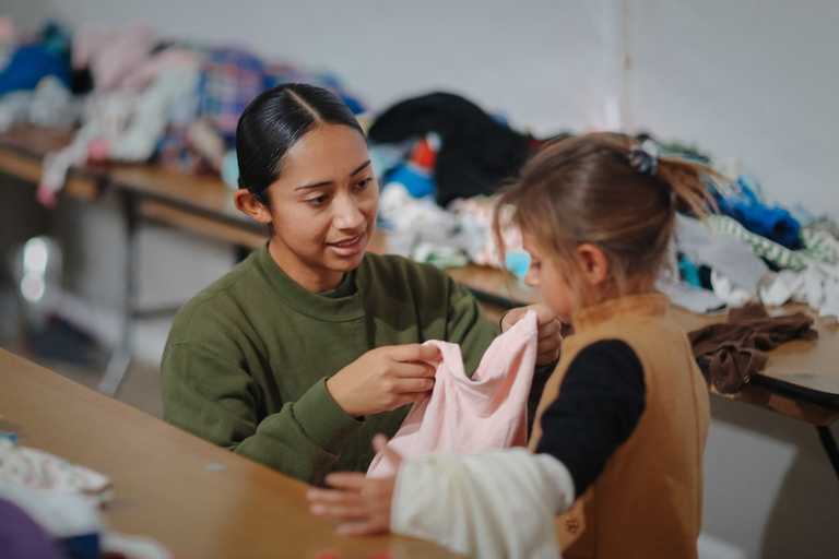 A volunteer holding up some clothes to a little girl to check for size