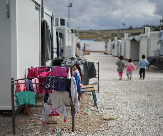 A refugee camp, with three young children with the backs turned walking in the distance