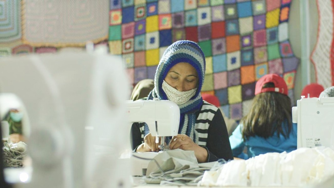 People in a room using sewing machines to create masks.